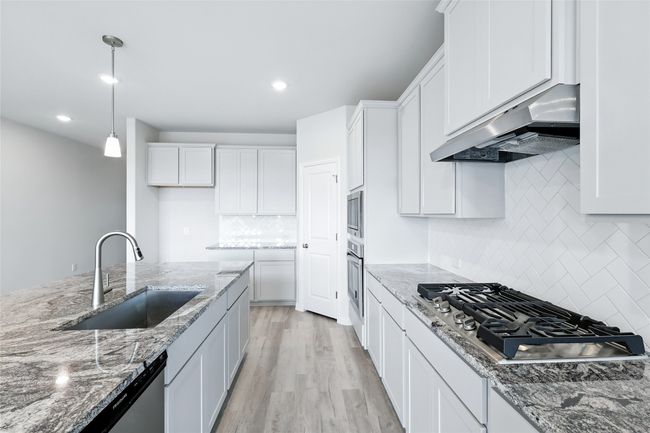 Kitchen with under cabinet range hood, stainless steel appliances, decorative backsplash, white cabinetry, and decorative light fixtures | Image 5