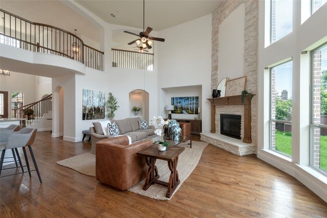 Living area with a high ceiling, arched walkways, a fireplace, wood finished floors, and a ceiling fan | Image 10