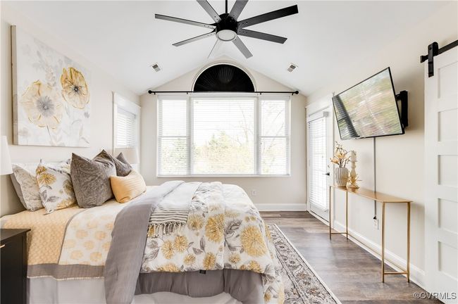Bedroom with visible vents, ceiling fan, wood finished floors, a barn door, and lofted ceiling | Image 36