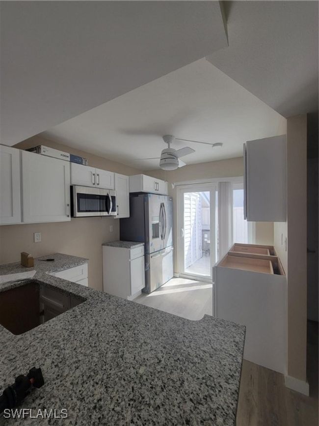 Kitchen with light wood-style flooring, white cabinetry, ceiling fan, refrigerator with ice dispenser, and light stone countertops | Image 14