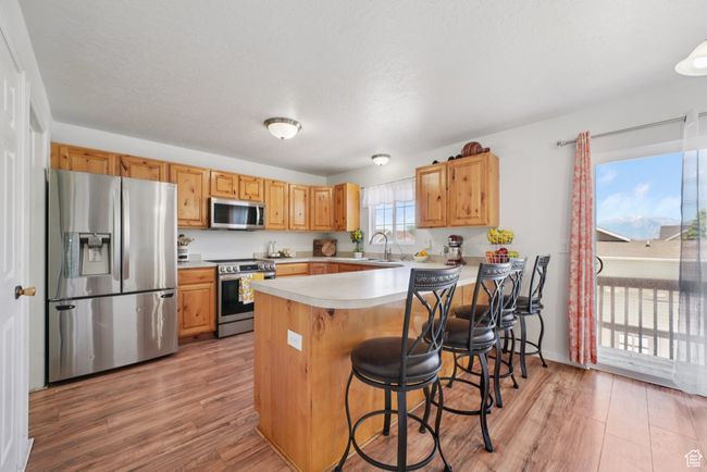 Kitchen featuring stainless steel appliances, light wood-type flooring, a peninsula, and light countertops | Image 8