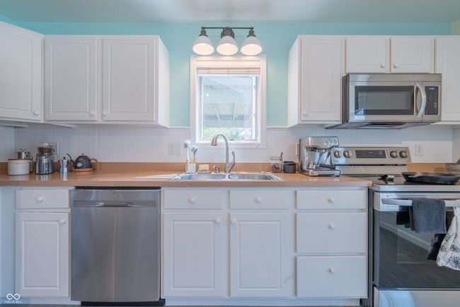 kitchen featuring stainless steel appliances, light countertops, a sink, and white cabinetry | Image 9