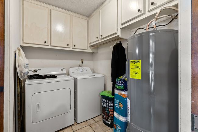 Laundry room with electric water heater, a textured ceiling, light tile patterned floors, washer and dryer, and cabinet space | Image 25