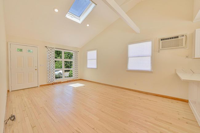 Spare room featuring a skylight, beamed ceiling, light wood-style floors, an AC wall unit, and high vaulted ceiling | Image 12