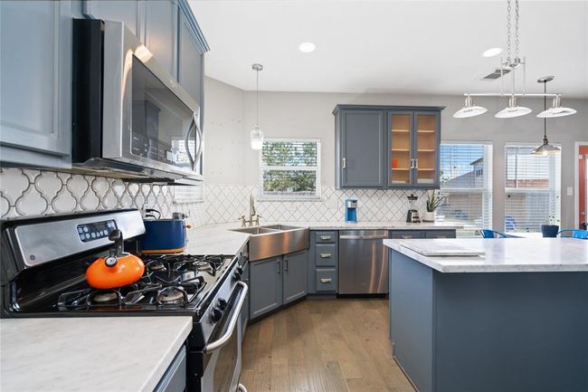 Modern kitchen with sleek gray cabinets, stainless steel appliances, and a spacious island. Features a stylish backsplash, pendant lighting, and ample natural light from large windows. Perfect for cooking and entertaining. | Image 28