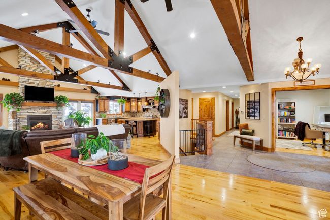 Dining space with high vaulted ceiling, beamed ceiling, light wood finished floors, a fireplace, and ceiling fan with notable chandelier | Image 6