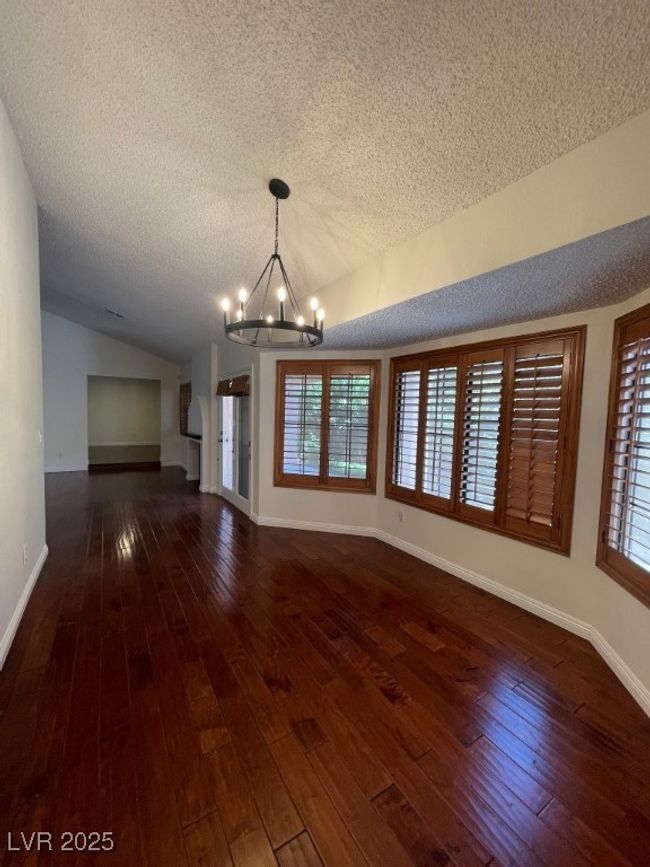 Unfurnished living room featuring a chandelier, a textured ceiling, vaulted ceiling, dark wood-type flooring, and healthy amount of natural light | Image 11