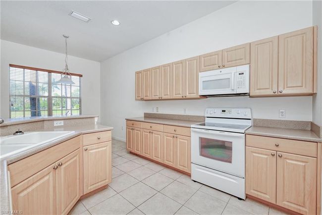 Kitchen with hanging light fixtures, light tile patterned floors, light brown cabinetry, and white appliances | Image 27