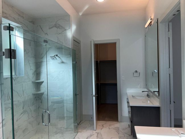 Bathroom featuring a stall shower, marble look tiles, vanity, and a walk in closet | Image 23