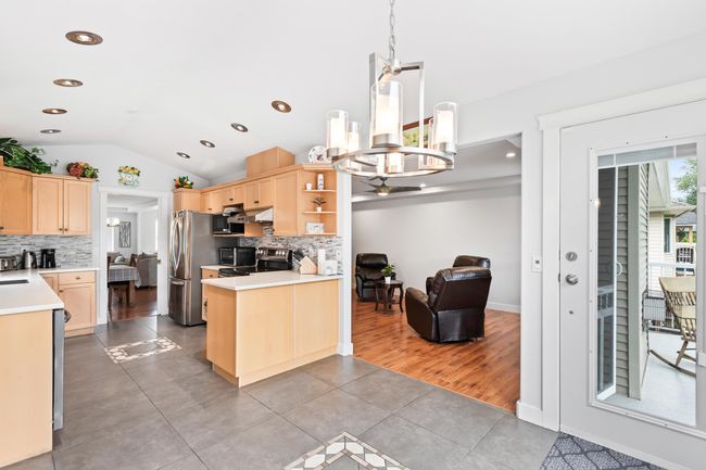 Kitchen with light brown cabinetry, tile patterned flooring, lofted ceiling, tasteful backsplash, and freestanding refrigerator | Image 12