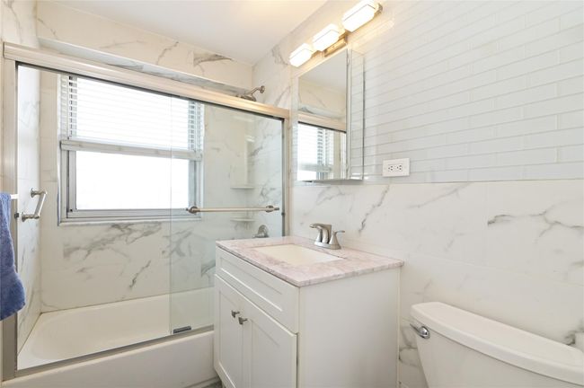 Full bathroom with tile walls, vanity, toilet, and shower / bath combination with glass door | Image 11