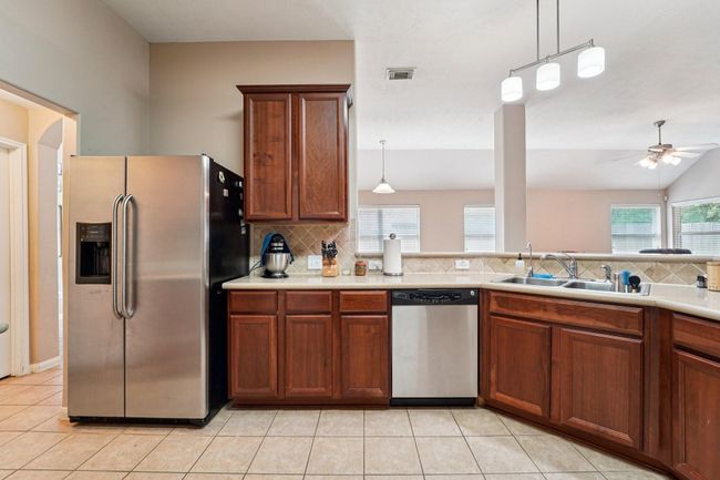 Another view of the kitchen features stainless steel appliances, including a side-by-side refrigerator and dishwasher. Warm wood cabinetry offers ample storage, while a spacious countertop and open layout provide a welcoming space for cooking and entertaining. | Image 8