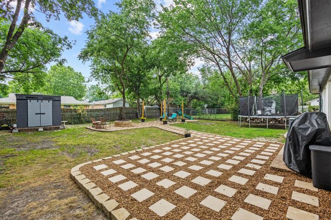 View of yard with a trampoline, a playground, a shed, an outdoor fire pit, and a patio | Image 11