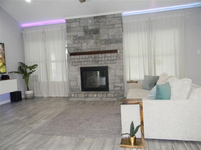 This living room features a cozy stone fireplace, modern ceiling fan, and sleek wood-look tile flooring. | Image 4