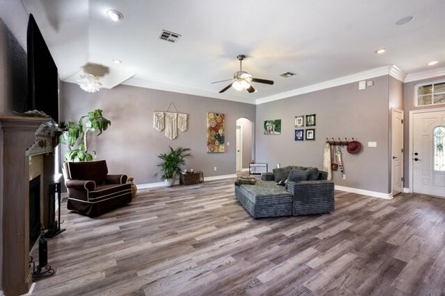 Living area with a fireplace, arched walkways, crown molding, a ceiling fan, and wood finished floors | Image 7