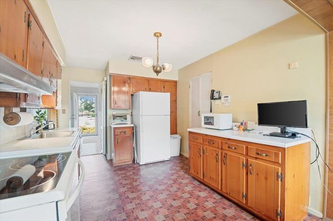 Kitchen with white appliances, ventilation hood, light countertops, and brown cabinets | Image 12