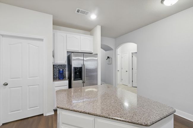 Kitchen featuring stainless steel fridge, arched walkways, a kitchen island, light stone countertops, and white cabinetry | Image 14