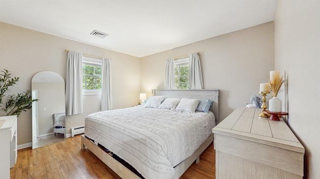 Very Large Bedroom featuring a baseboard heating units, multiple windows and light stained hardwood flooring. | Image 15