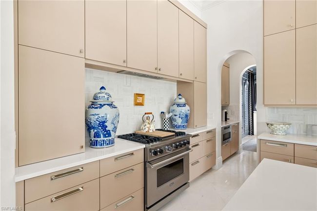 Kitchen with tasteful backsplash, arched walkways, stainless steel appliances, light countertops, and cream cabinetry | Image 15