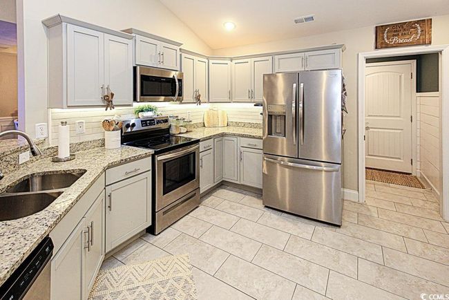 Kitchen featuring sink, appliances with stainless steel finishes, light stone countertops, decorative backsplash, and vaulted ceiling | Image 13
