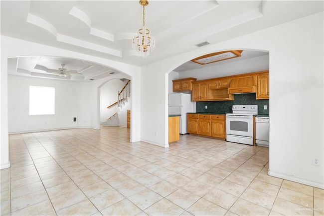 Kitchen with a tray ceiling, white appliances, open floor plan, arched walkways, and light tile patterned flooring | Image 7