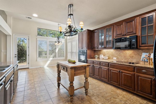 This spacious kitchen is a chef’s dream, featuring rich stained wood cabinets, sleek black appliances, and an abundance of counter and cabinet space. | Image 12