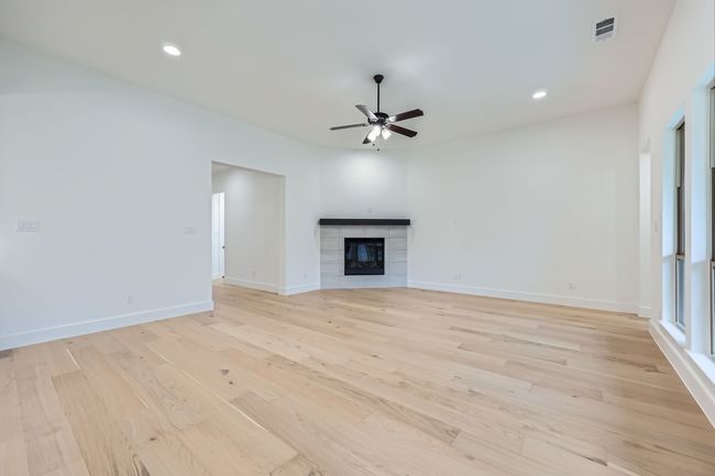 Unfurnished living room featuring a ceiling fan, a tile fireplace, light wood-style flooring, and visible vents | Image 4