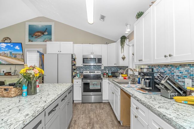 Kitchen with stainless steel appliances, a sink, vaulted ceiling, light wood-style floors, and decorative backsplash | Image 9