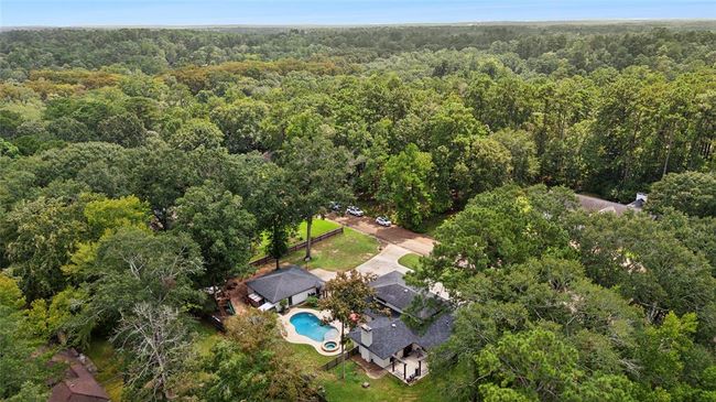 This aerial photo showcases a spacious home surrounded by dense greenery, offering privacy and tranquility. The property features a pool and a large driveway, nestled in a forested setting. Ideal for those seeking a serene retreat. | Image 5