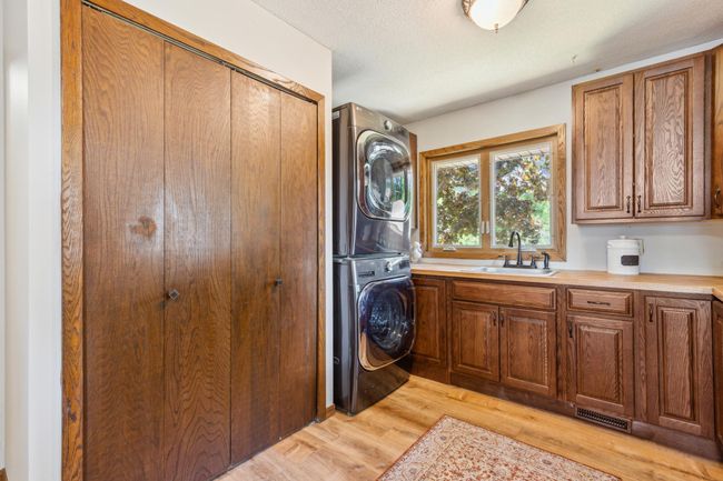 Spacious laundry area featuring modern stacked washer and dryer, ample cabinetry, a utility sink, and large window for natural light. | Image 14