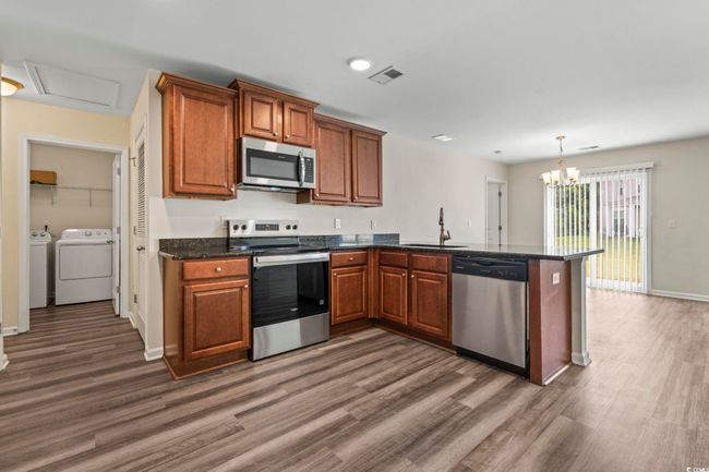 Kitchen featuring washer and clothes dryer, stainless steel appliances, a peninsula, and brown cabinets | Image 9