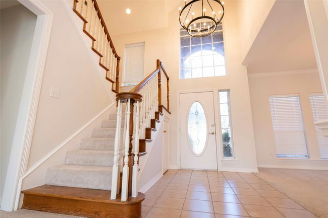 Entrance foyer with a chandelier, stairway, tile patterned floors, carpet floors, and a high ceiling | Image 8