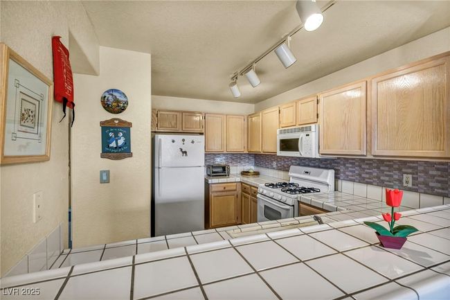 Kitchen with light brown cabinetry, a toaster, tasteful backsplash, white appliances, and tile countertops | Image 31