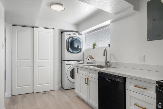 Laundry room featuring stacked washer / dryer, electric panel, light wood-style flooring, and a textured ceiling | Image 9