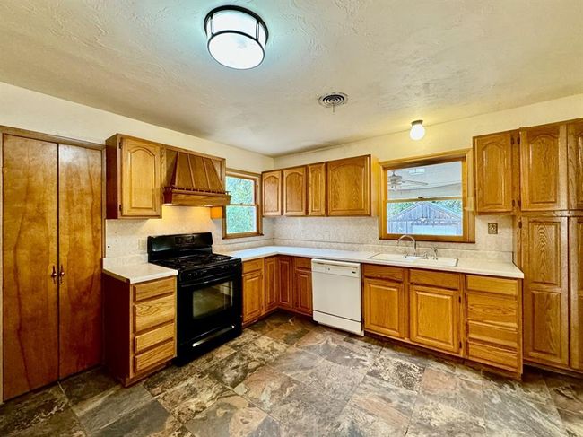 Kitchen featuring gas stove, white dishwasher, premium range hood, light countertops, and dark stone finish flooring | Image 8