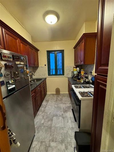 Kitchen featuring stainless steel fridge, backsplash, white gas range oven, sink, and dark stone counters | Image 1