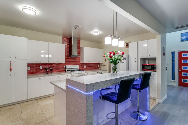 Kitchen with white appliances, wall chimney exhaust hood, decorative backsplash, a center island, and pendant lighting | Image 10
