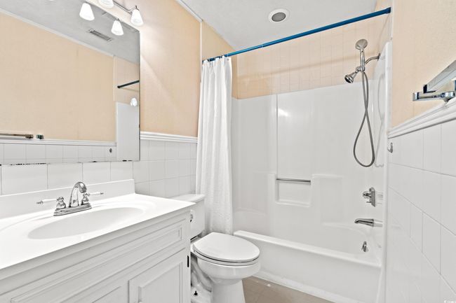 Full bath featuring tile walls, vanity, shower / bath combo with shower curtain, wainscoting, and tile patterned flooring | Image 16