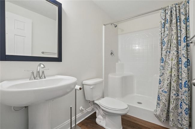 Bright and functional lower-level full bathroom featuring a pedestal sink, chrome fixtures, and a walk-in shower with built-in seating. Clean white finishes and wood-look LVP flooring create a fresh and welcoming space. | Image 34