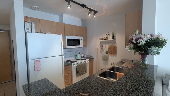 Kitchen featuring a sink, open shelves, light brown cabinetry, white appliances, and dark countertops | Image 9