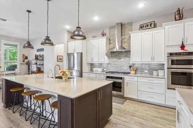 Kitchen with wall chimney range hood, appliances with stainless steel finishes, light wood tile flooring, decorative backsplash, and recessed lighting | Image 13