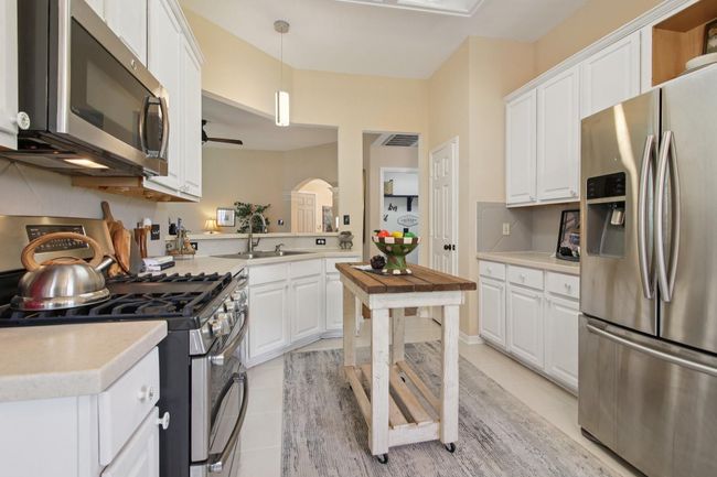 This kitchen features modern stainless steel appliances and white cabinetry. It has ample counter space and a cozy, open layout with warm lighting. | Image 11