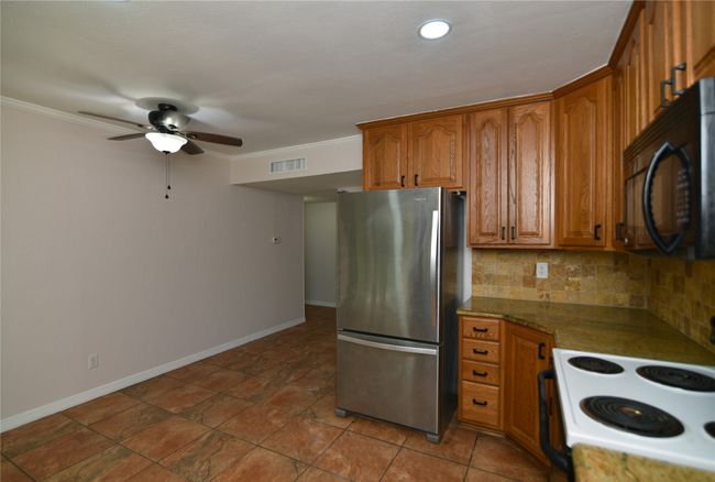 Kitchen with dining, freestanding refrigerator, black microwave, electric range, ceiling fan, and brown cabinetry | Image 12