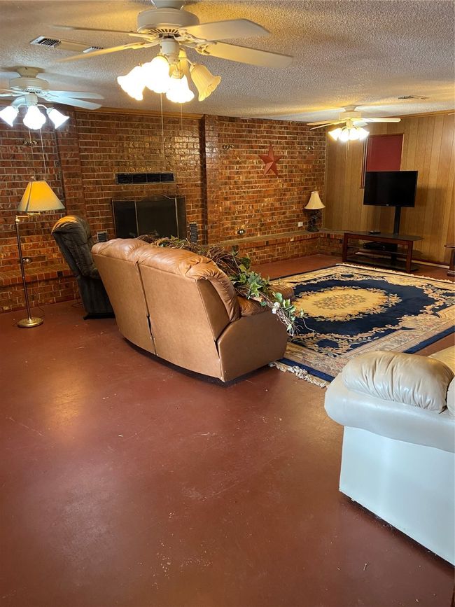 Living room with ceiling fan, a textured ceiling, and brick wall | Image 10