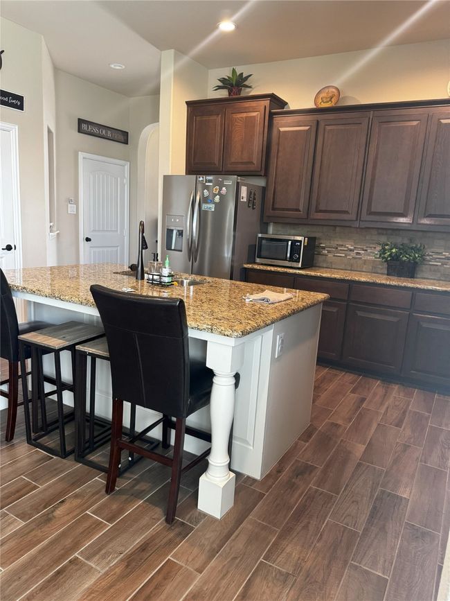 Kitchen with stainless steel appliances, dark wood finished floors, arched walkways, a kitchen island with sink, and recessed lighting | Image 19