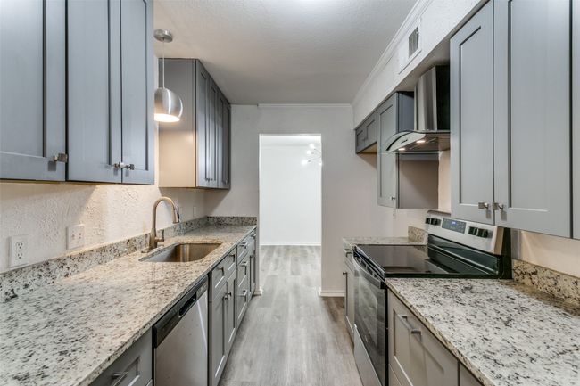 Kitchen with wall chimney range hood, light stone counters, a sink, light wood-style floors, and stainless steel appliances | Image 10