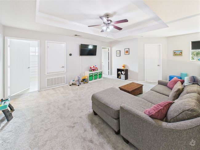 Carpeted living room with a tray ceiling, ceiling fan, and crown molding | Image 16