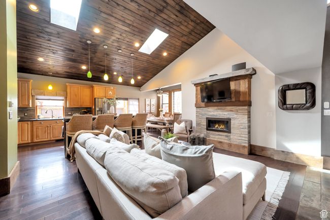 Living area with dark wood-style flooring, high vaulted ceiling, a stone fireplace, wood ceiling, and a skylight | Image 6
