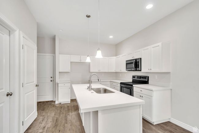 Kitchen featuring appliances with stainless steel finishes, light wood finished floors, white cabinets, an island with sink, and pendant lighting | Image 12