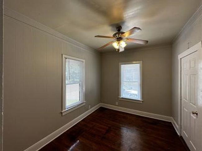 Empty room with healthy amount of natural light, dark wood-style flooring, crown molding, and ceiling fan | Image 8